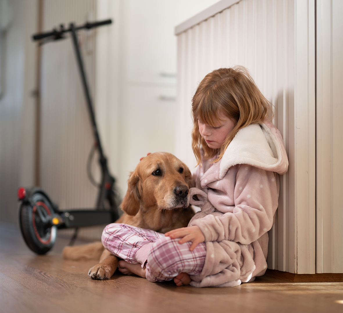 Jente som sitter med hund og elsparkesykkel til lading. Foto.
